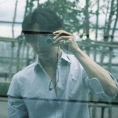 a man taking a photo with his camera in front of a glass wall and trees