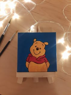 a painting of winnie the pooh on a small easel with lights in the background