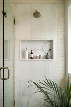 a white tiled bathroom with shelves and plants in the corner, along with a glass shower door