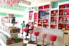 two girls are standing in the candy shop with pink stools and red shelving