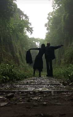 two people standing in the middle of a forest with their arms spread out to each other