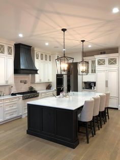 a large kitchen with white cabinets and black island in the center is lit by pendant lights