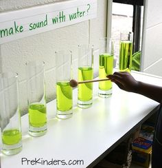 a person holding a wooden stick in front of some glasses with green liquid on them