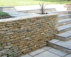 a stone wall with steps leading up to it and a potted plant in the corner