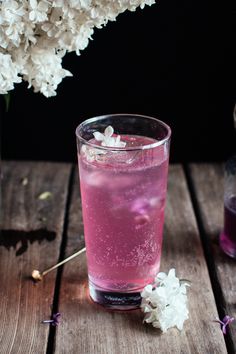 a glass filled with pink liquid next to white flowers