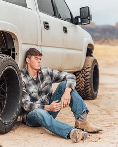 a young man sitting in front of a truck with his foot on the ground next to it