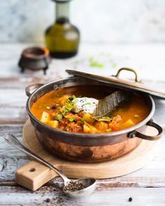 a bowl of soup on a wooden board with a spoon and bottle in the background