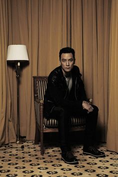 a man sitting on top of a chair next to a lamp and curtained wall