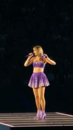 a woman standing on top of a stage with a microphone in her hand and wearing a purple outfit