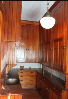 an empty kitchen with wooden cabinets and wood flooring on the walls, along with a hanging light fixture