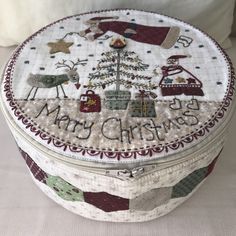 a small round box with christmas decorations on the front and side, sitting on a bed