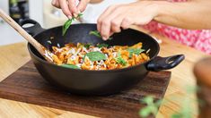 a woman cooking pasta in a skillet on top of a wooden cutting board with a wooden spoon