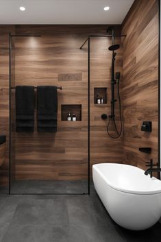 a modern bathroom with wood paneling and black accents on the walls, along with a freestanding tub