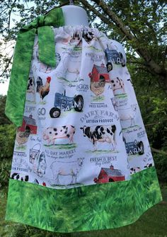 a dress hanging from a tree with farm animals on it and green trim around the neck