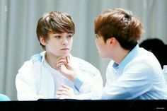 two young men sitting at a table with one holding his hand to the other's chin