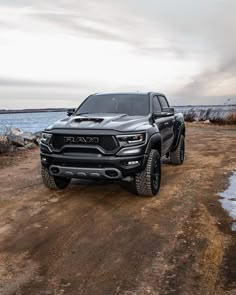 a black truck parked on top of a dirt road next to the ocean and snow covered ground