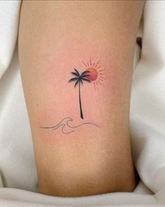 a small palm tree on the side of a woman's leg with waves and sun behind it