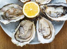 a white plate topped with oysters on top of a wooden table next to a slice of lemon