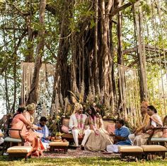 a group of people sitting around each other in front of a large banyan tree