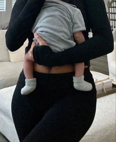 a woman holding a baby in her arms while wearing black pants and a gray shirt