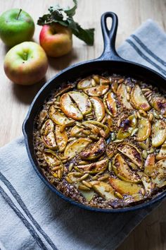 a skillet filled with food sitting on top of a wooden table next to apples