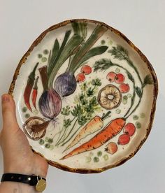 a hand holding a plate with vegetables painted on it