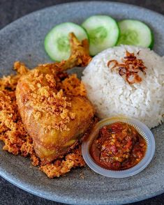 a plate with rice, chicken and cucumber slices on it next to some sauce