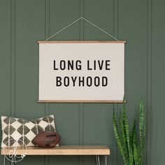 a sign that says long live boyhood hangs on a wall next to a plant