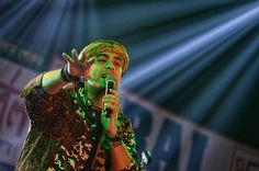 a man holding a microphone in his right hand and wearing a green outfit on stage