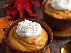 two small bowls filled with pumpkin pudding on top of a wooden table next to autumn leaves