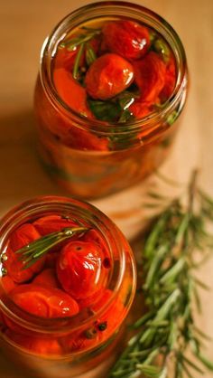 two jars filled with pickled tomatoes on top of a wooden table