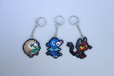 three pixel keychains are sitting on a white surface, each with an image of the same character