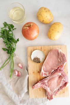 raw meat on cutting board next to garlic, onion, and potatoes with dressing in glass bottle