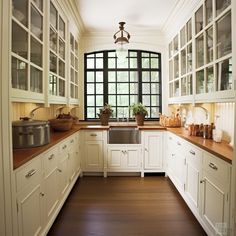 a kitchen with wooden floors and white cabinets, windows, and pots on the counter