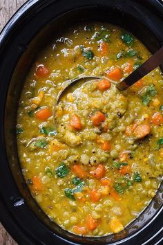 a crock pot filled with vegetable soup and a wooden spoon in the bowl next to it