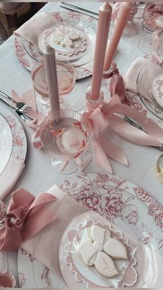 the table is set with pink and white plates, silverware, and candy hearts