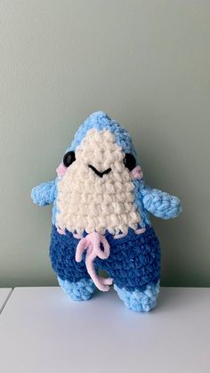 a crocheted blue and white stuffed animal sitting on top of a table next to a green wall