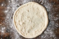 an uncooked pizza dough sitting on top of a wooden table covered in powdered sugar