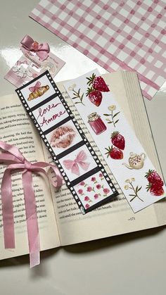 an open book with pink ribbon on top of it and some other items in the background