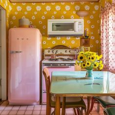 a pink refrigerator sitting next to a table with yellow flowers in a vase on top of it