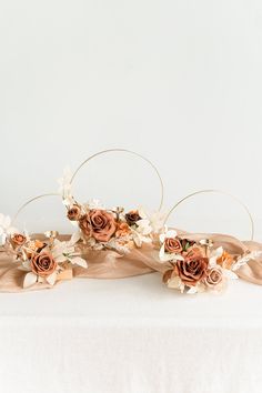 three wedding headpieces with flowers and leaves on top of a white table cloth