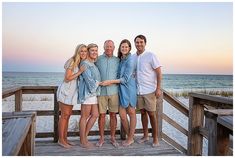 a group of people standing on top of a wooden deck next to the ocean at sunset