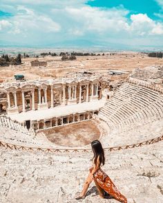 a woman sitting on the ground in front of an old amphith with columns