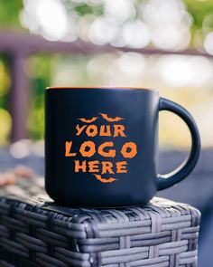 a black coffee mug sitting on top of a wicker basket that says your logo here