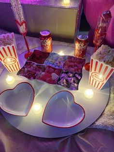 a table topped with two heart shaped trays filled with candy and candies next to candles