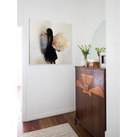 a painting hangs on the wall next to a dresser with a mirror and vase in it