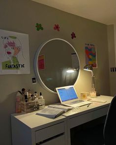 a laptop computer sitting on top of a desk next to a round mirror and lamp