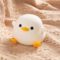 a white plastic toy with black eyes and yellow feet sitting on a beige fabric covered surface