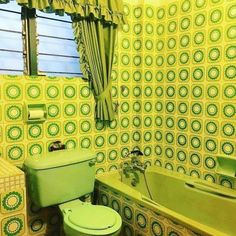 a green toilet sitting next to a bath tub in a room with yellow walls and curtains