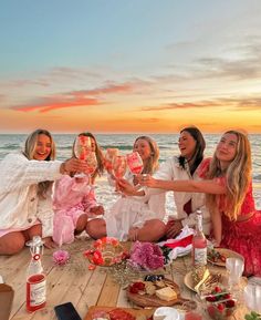 a group of women sitting on top of a wooden floor next to the ocean at sunset